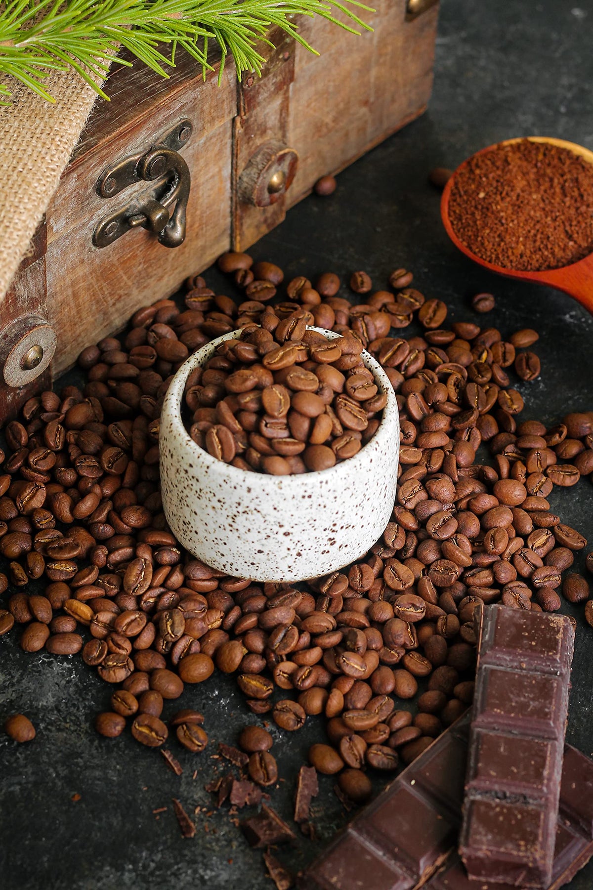Roasted specialty coffee beans with ground coffee and chocolate on a dark tabletop